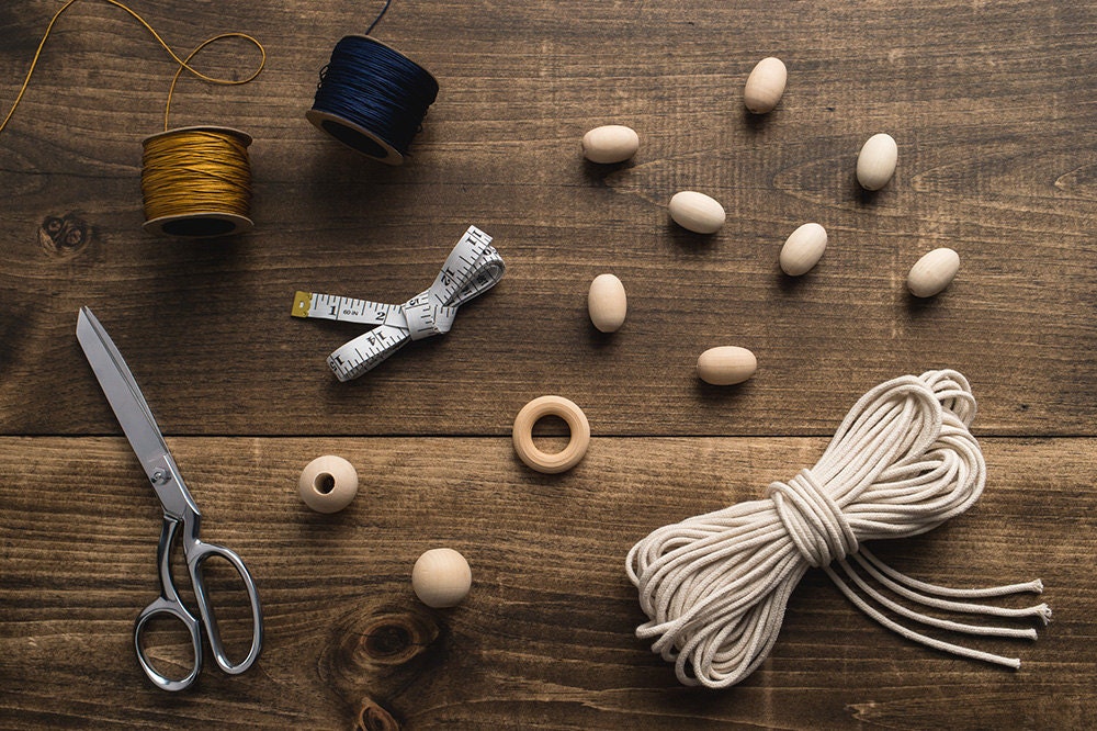 All the supplies you need to make a DIY macrame-inspired plant hanger, including beads, scissors, cord, and a measuring tape.