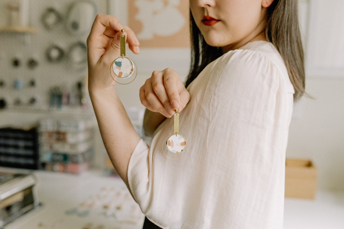 Elyse holds up a pair of dangly terrazzo earrings from her latest collection