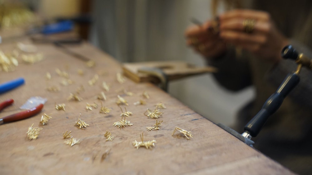 A closeup of Maria's hands as she works on assembling rows of botanical post earrings