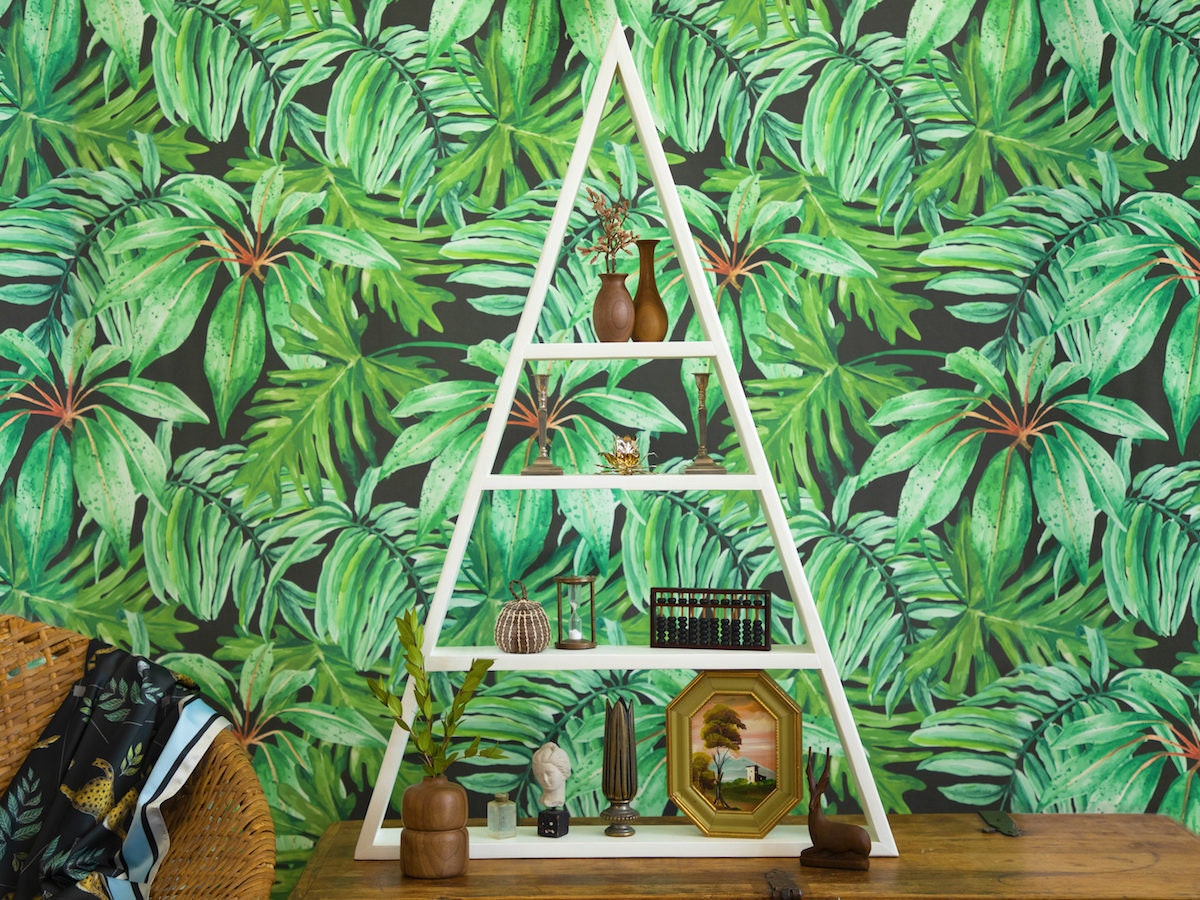 A shelf styled with natural and vintage accents and displayed in front of bold, tropical wallpaper