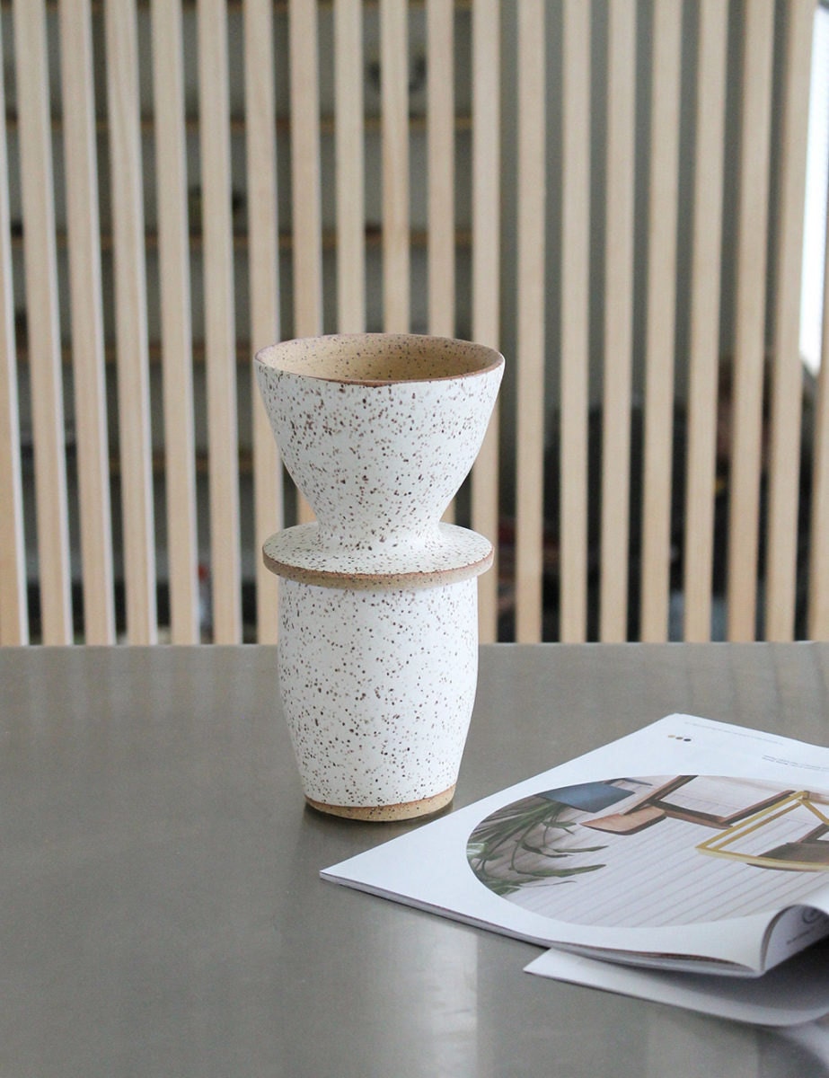 A speckled ceramic cup with a matching pour-over coffee setup on top.