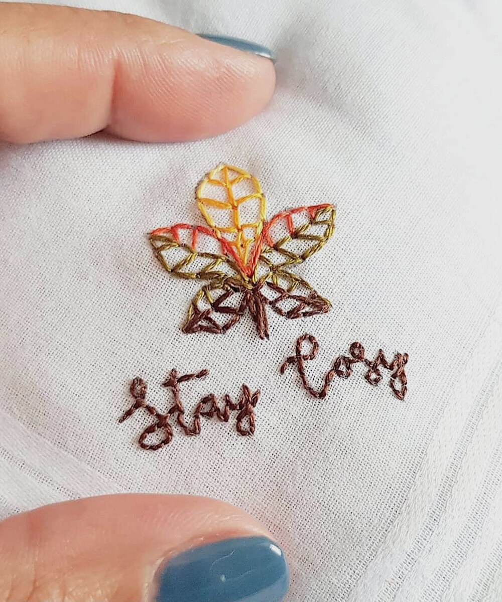 Close up detail on an embroidered leaf with the words "Stay cozy"