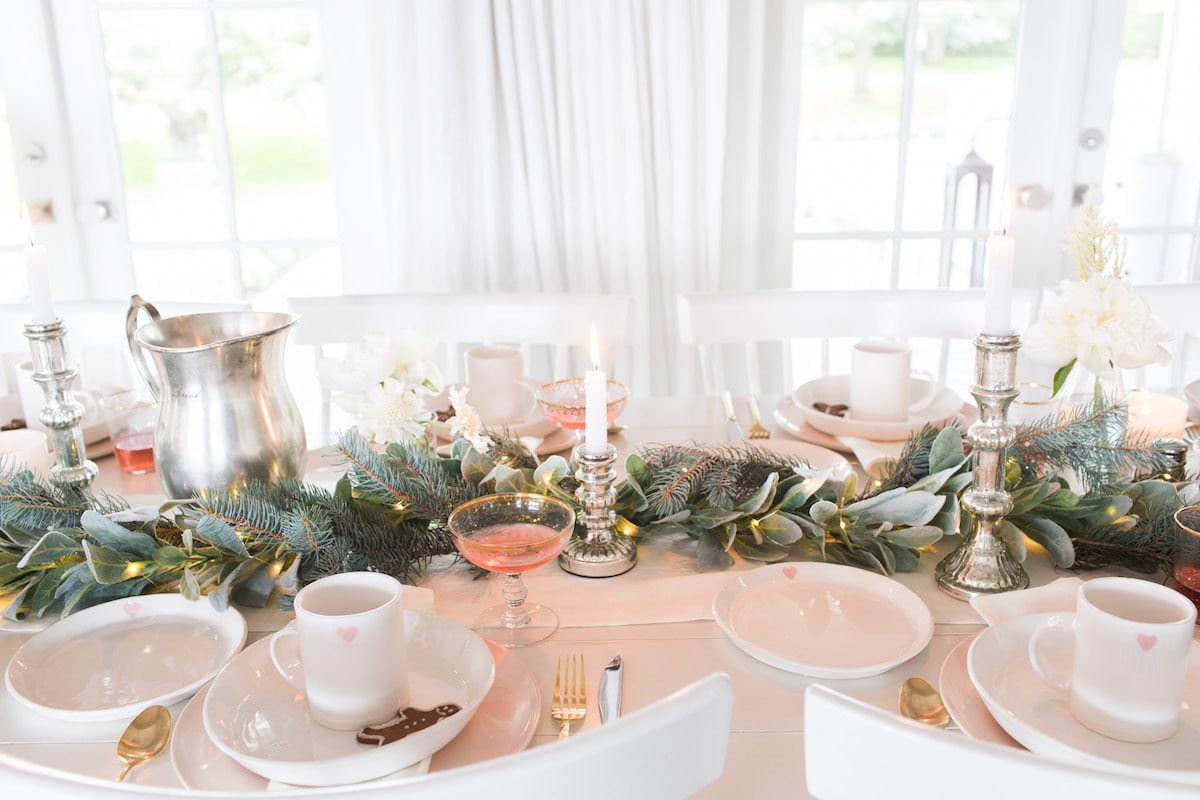 Holiday tabletop with mixed greenery, white ceramic plates, and festive metallic accents