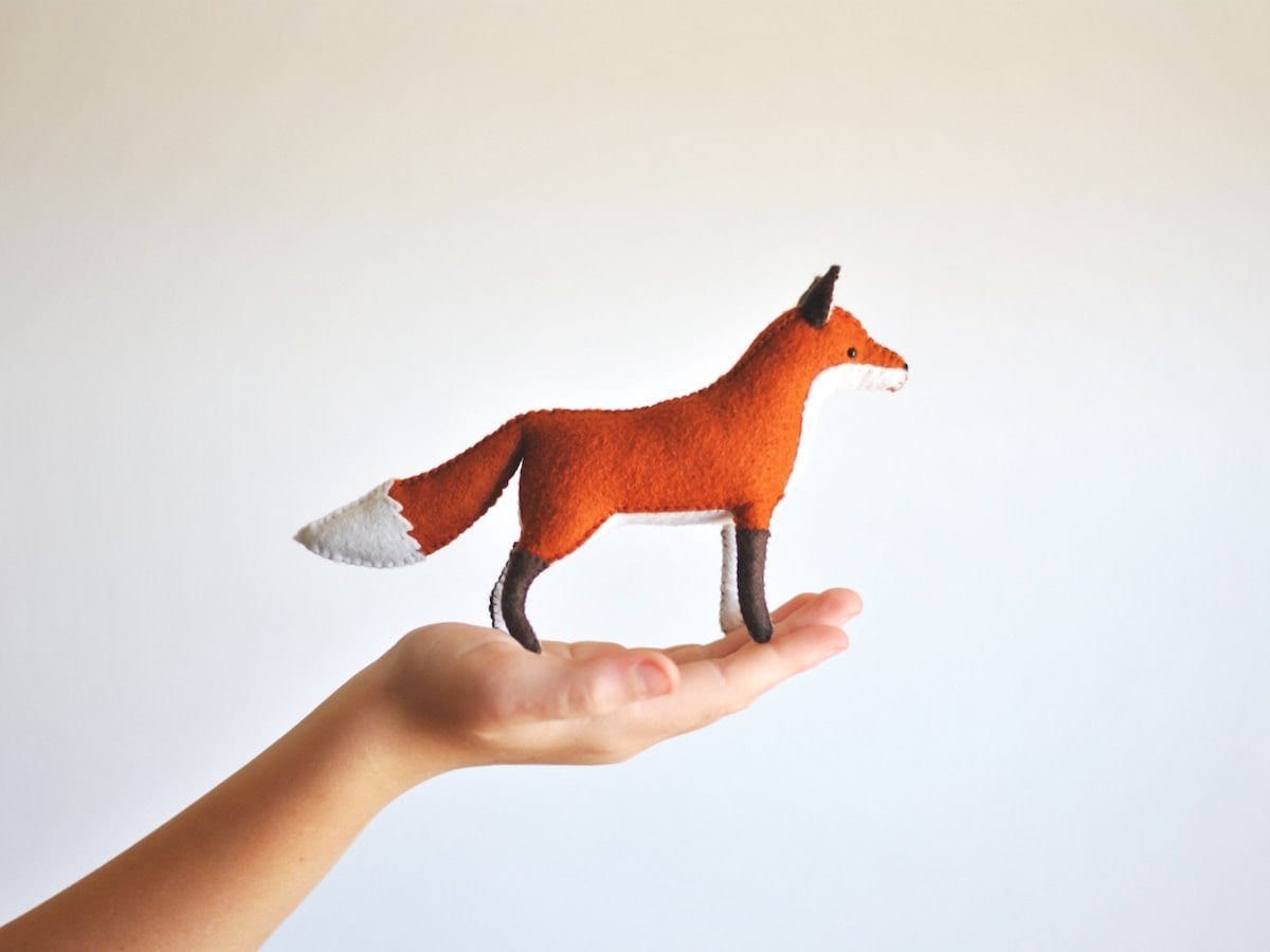 A hand-sewn stuffed felt fox resting in the palm of a person's hand