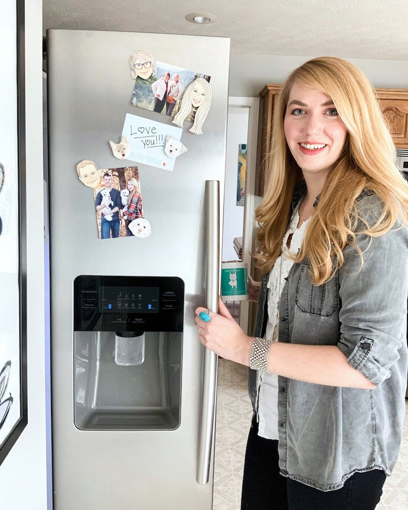 Brittney standing in her kitchen holding her fridge door open with personalized magnets on display