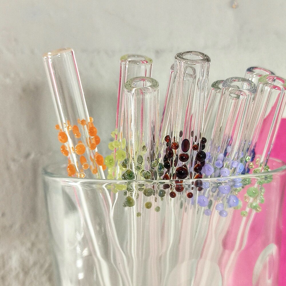 A glass cup filled with a set of reusable glass drinking straws decorated with colorful dots from Scarlet Impressions.