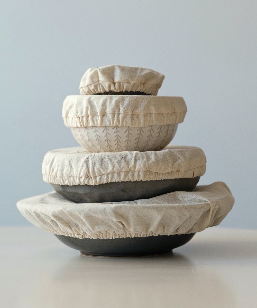 A set of natural-colored reusable linen bowl covers shown covering bowls of various sizes.