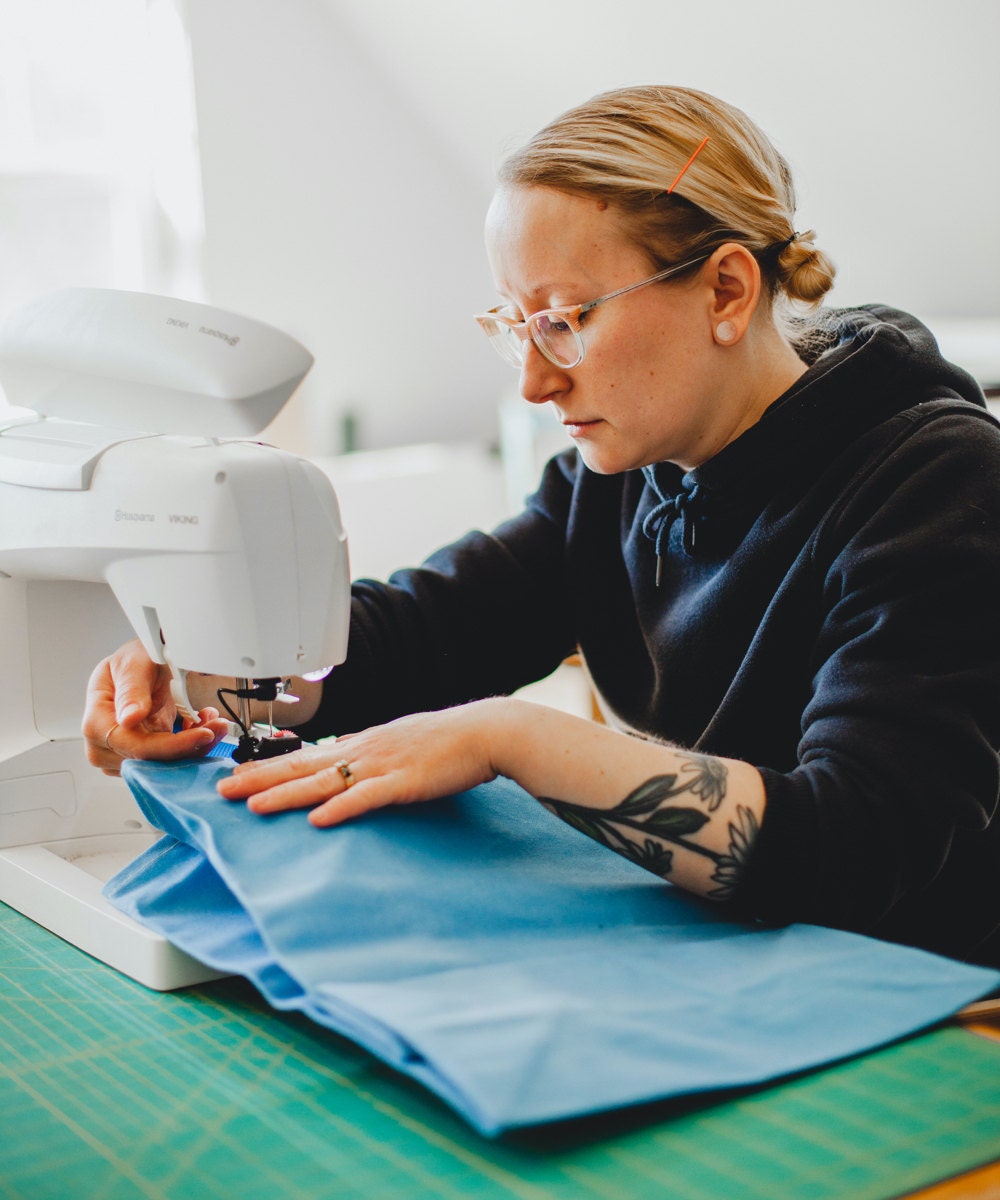 Hanna sews a strap onto a blue market bag.