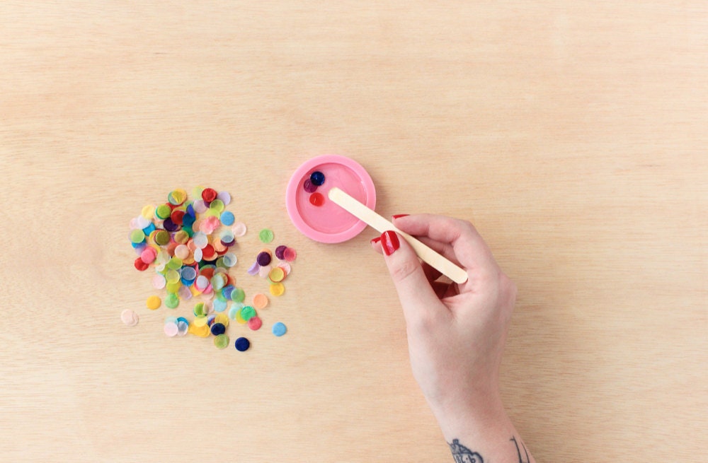 Rachel pushes individual pieces of confetti into her resin mold with a wooden stick.