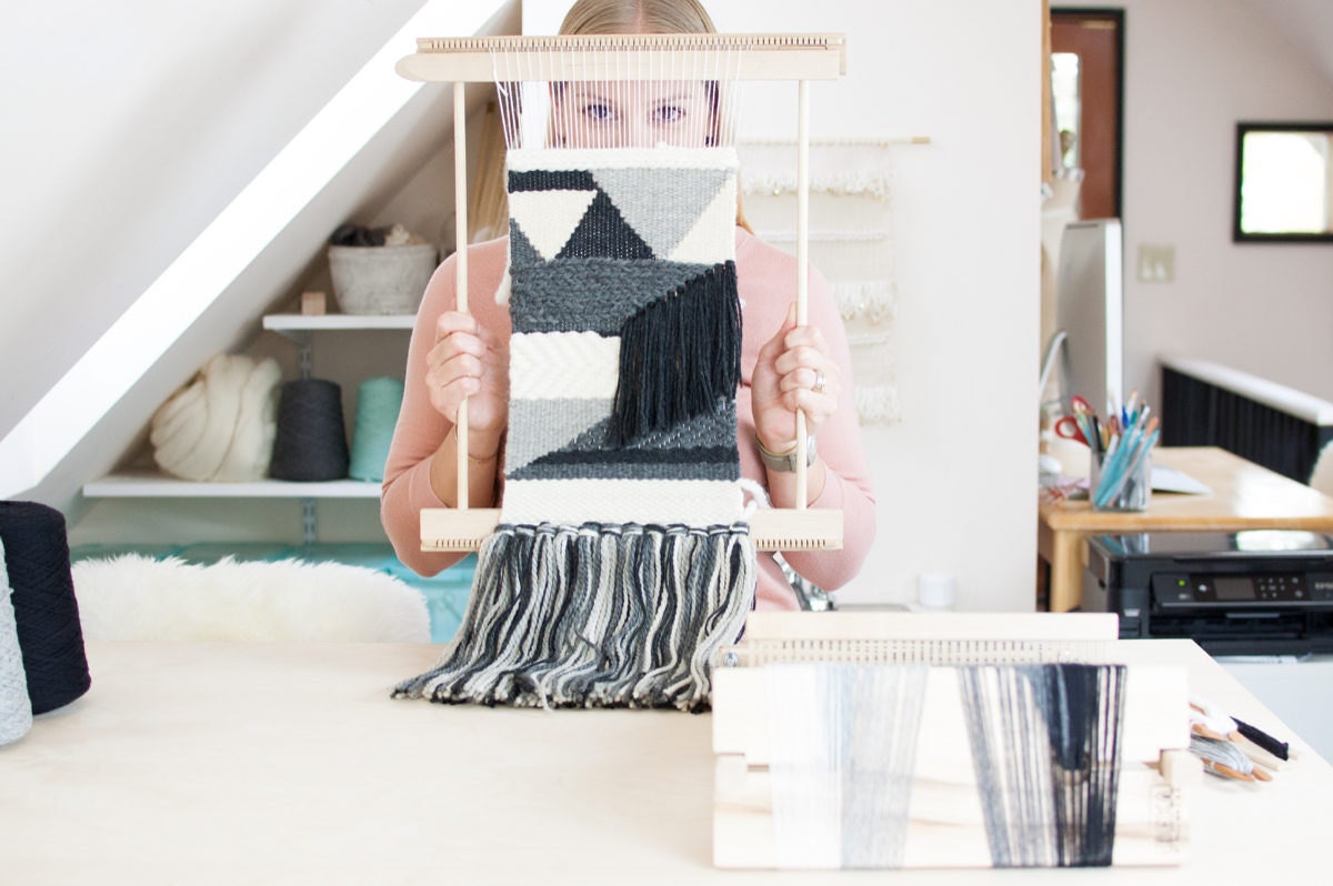 Ashley holds up a WIP weaving on a loom.