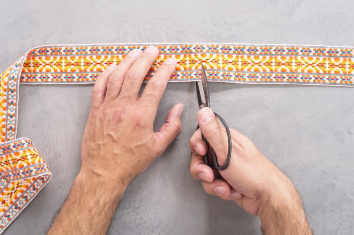 Hands cutting fabric trim with steel shears at desired length