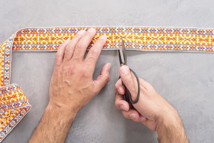 Hands cutting fabric trim with steel shears at desired length