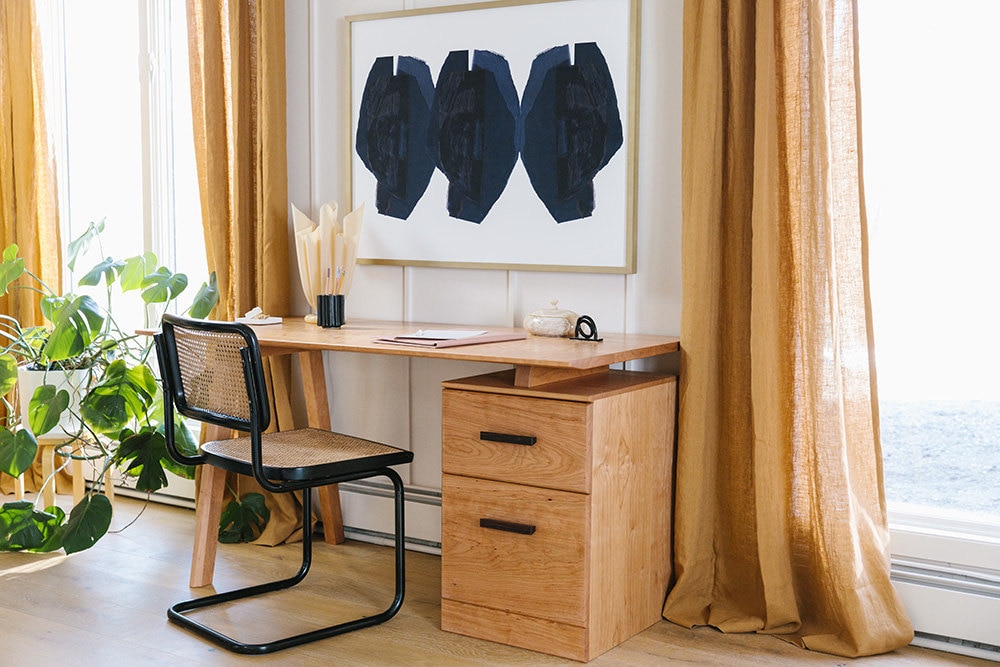 Windows with long amber curtains flank a wooden desk with drawers and a surface that appears to be floating.