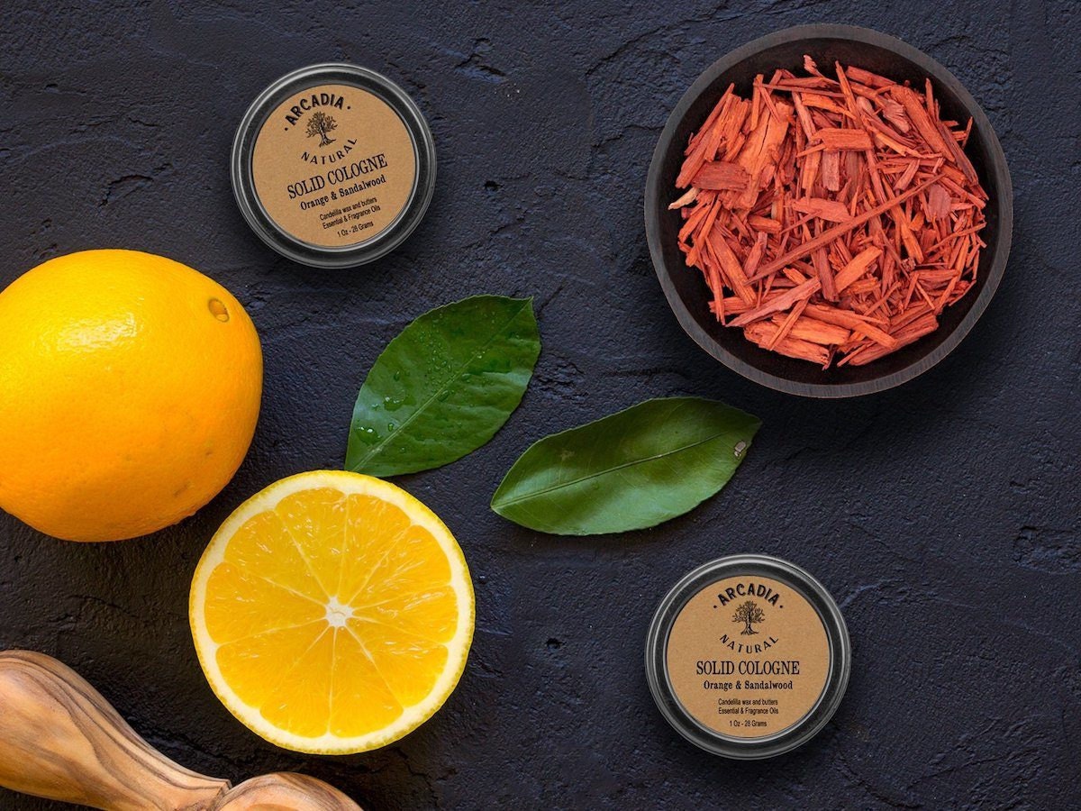 Solid cologne displayed on a table with sandalwood chips and oranges.