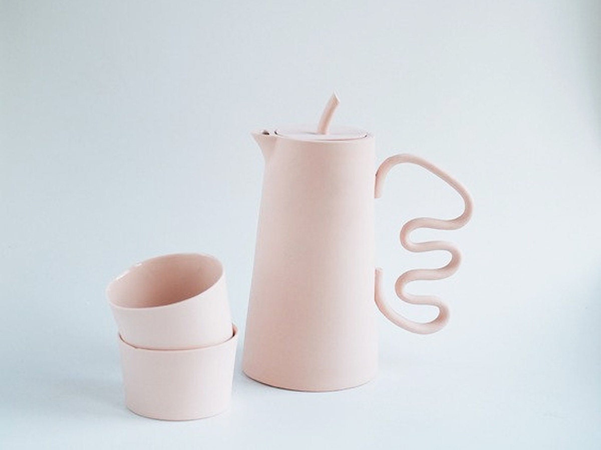 A pink tea set and pitcher with a wavy handle