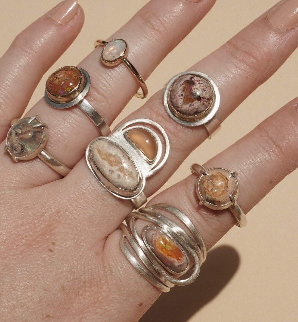 Assorted opal statement rings from Aleishla styled on a hand.
