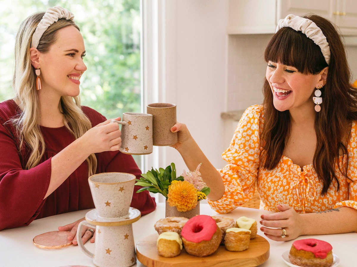 Elsie and Emma cheers with mugs at a kitchen table