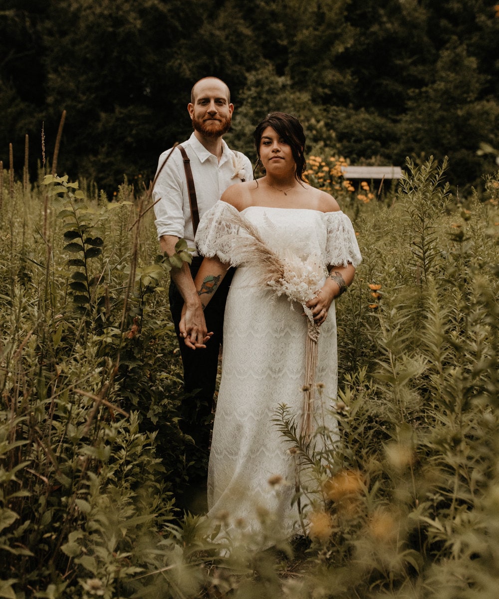 A portrait of Sarah and Chris Schalago standing in a meadow on their wedding day.