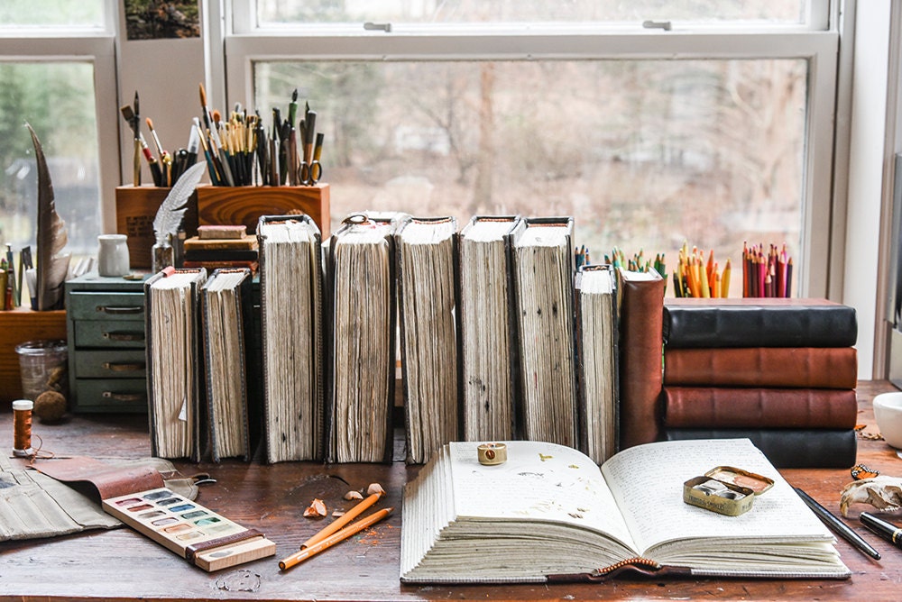 A desk decorated with bound books, desk caddies, and a painter's palette.