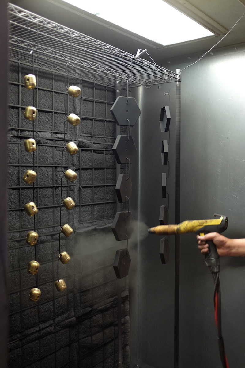 Kyle sprays the finish onto a string of brass lighting components