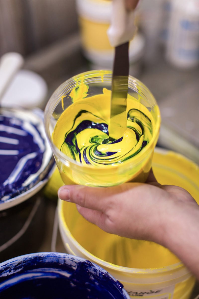 Mixing yellow and blue paints to create a specific shade for screenprinting.