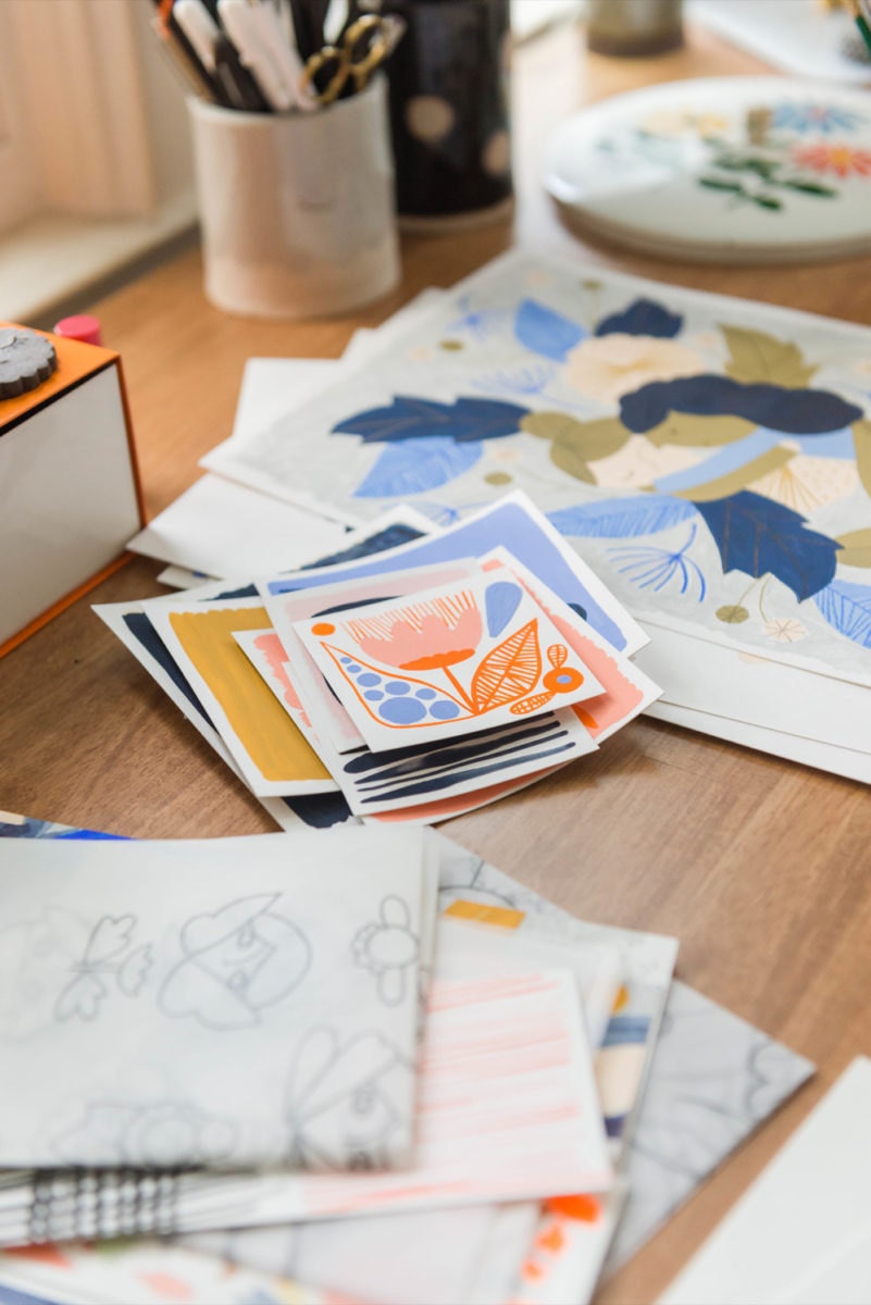 Assorted cards and illustrated prints stacked on Meenal's desk