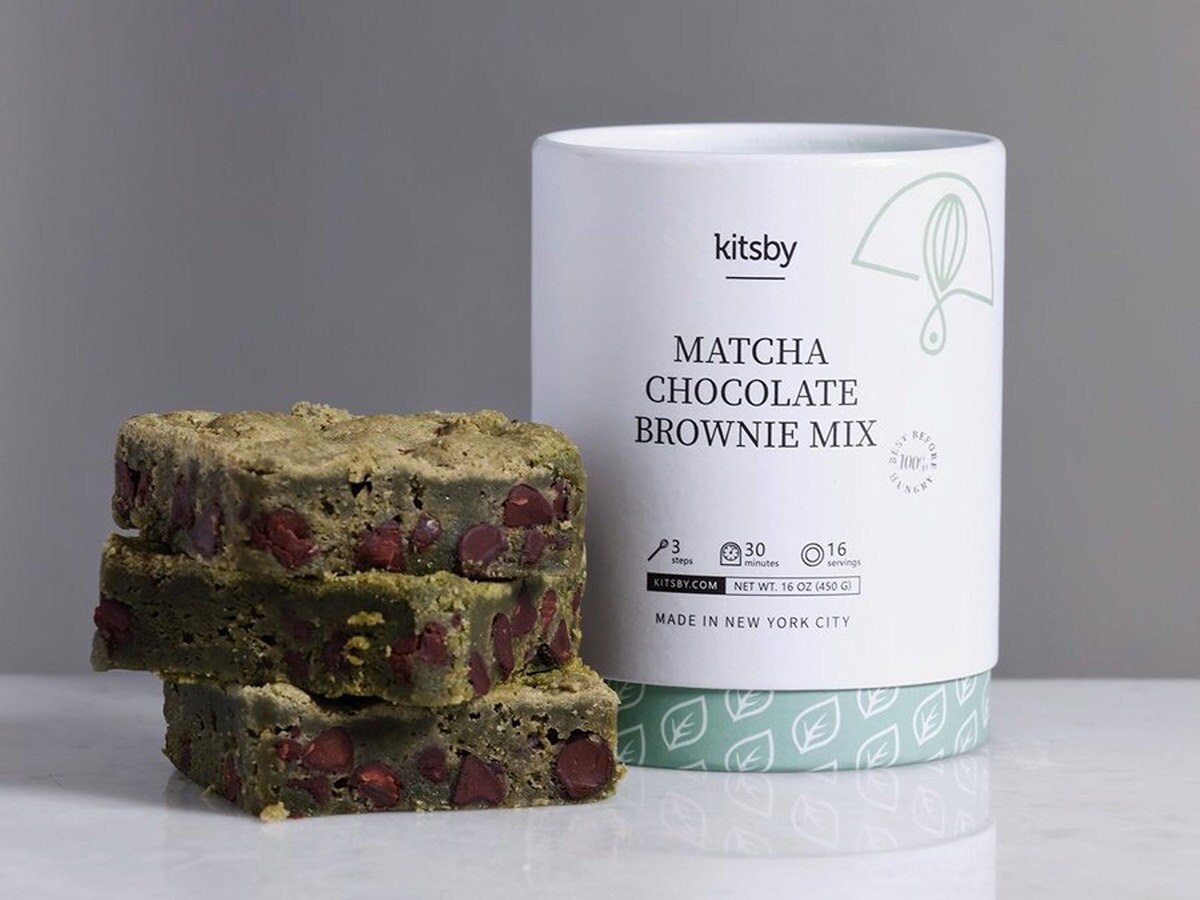 Three matcha chocolate brownies next to a package of the mix to make them.