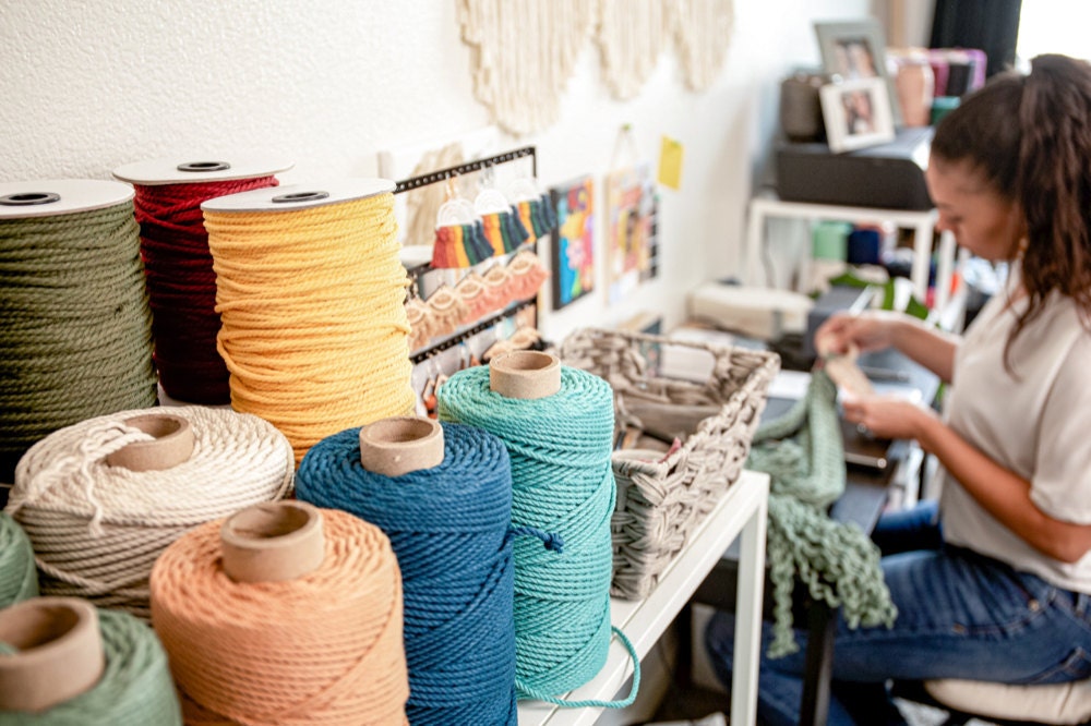 Case works on a macrame plant hanger at her desk, surrounded by colored cord and other materials.