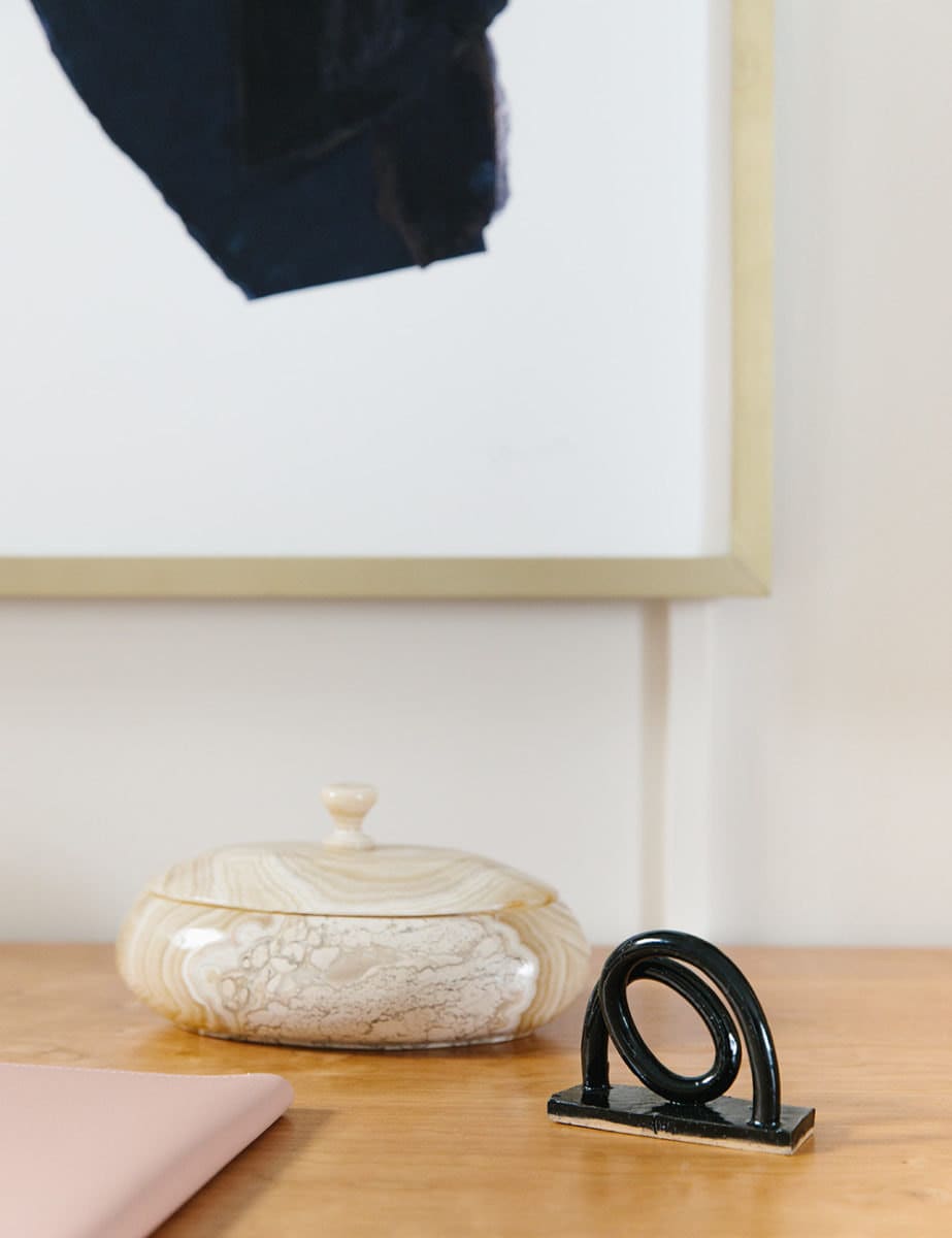 An onyx lidded dish and a swirly ceramic figurine sit atop a wooden desk.