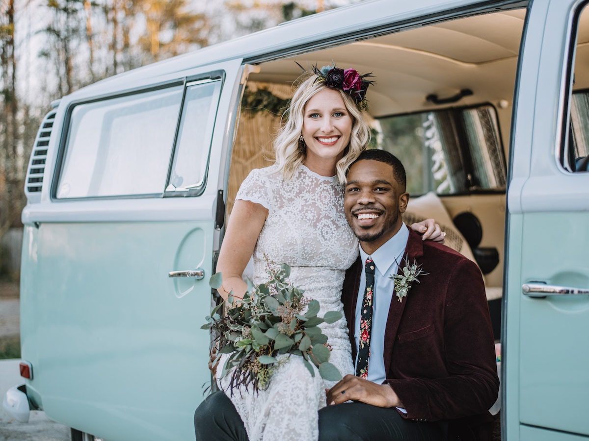 A bride and groom pose together in front of a blue Volkswagen van-turned photo booth.