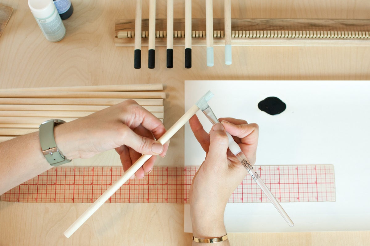 Ashley paints the tips of wooden dowels that will be come hanging rods for her loom kits.