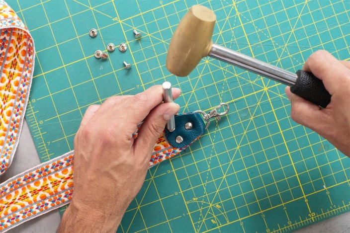 For the final step in this DIY camera strap, rivets are set in each of the three holes using a mallet and rivet setter