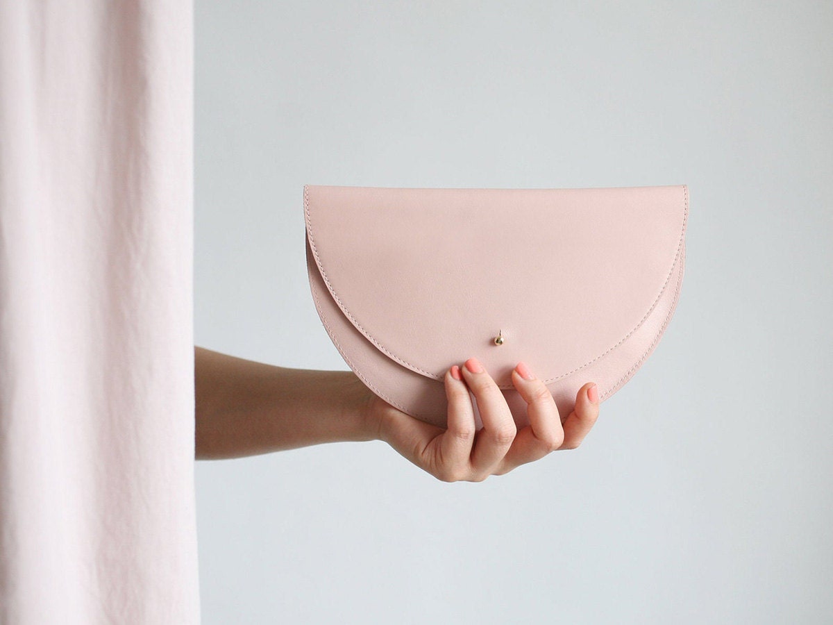 A model holds a half-moon shaped clutch in pastel pink.