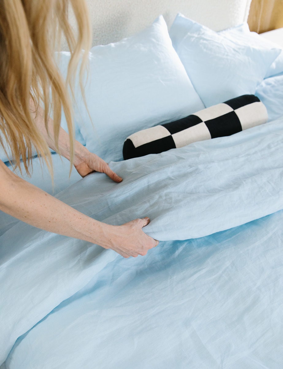 Sarah makes the bed with a sky blue linen duvet and a black-and-white checkered bolster pillow.