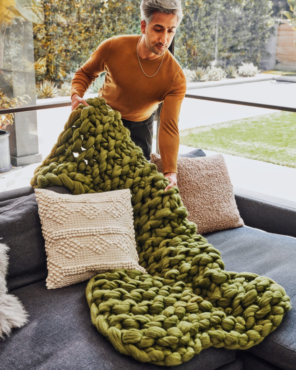 Tan lays an olive green chunky knit throw blanket from the Tan France x Etsy collection on a couch