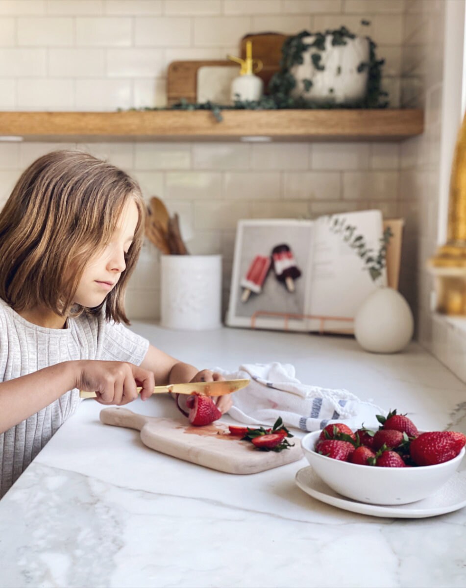 One of Kristine's daughters slices strawberries on a maple wood cutting board.