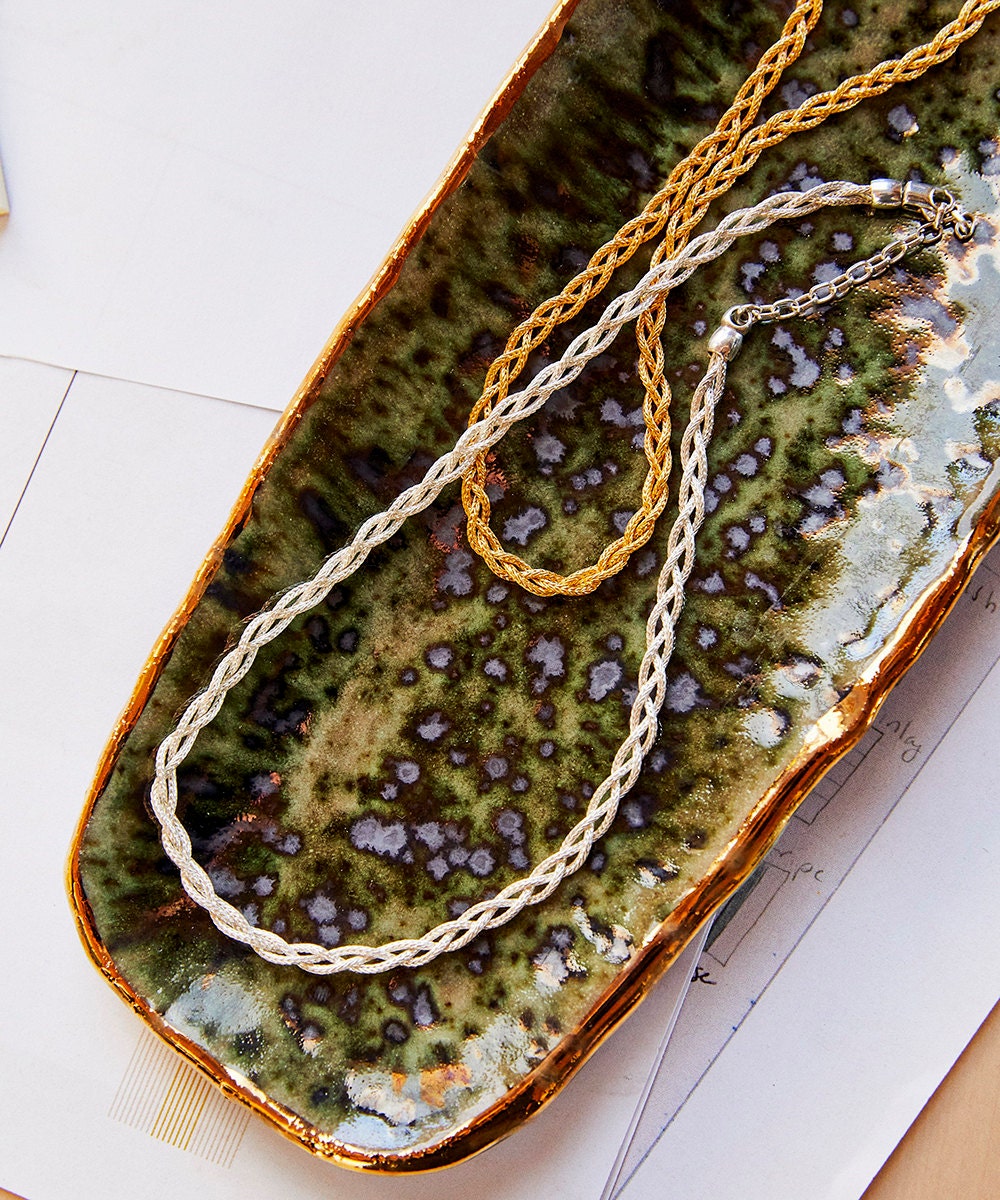 A gold chain and a silver chain in a green dish.