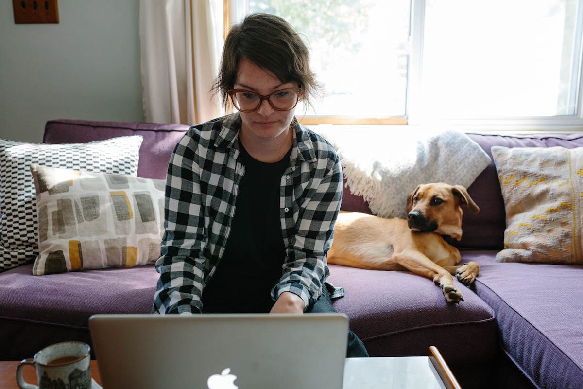 Brenda sitting on her couch with her dog, working on her computer