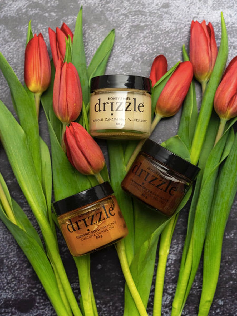 Three jars of honey against a stone backdrop with tulips.