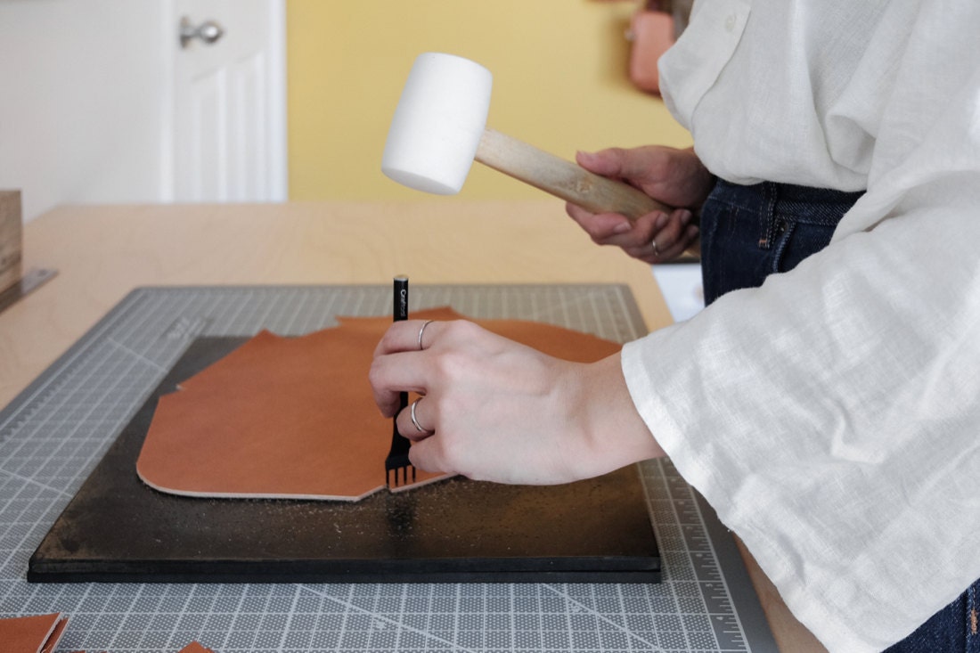 Quynh uses a mallet to make holes in a piece of leather