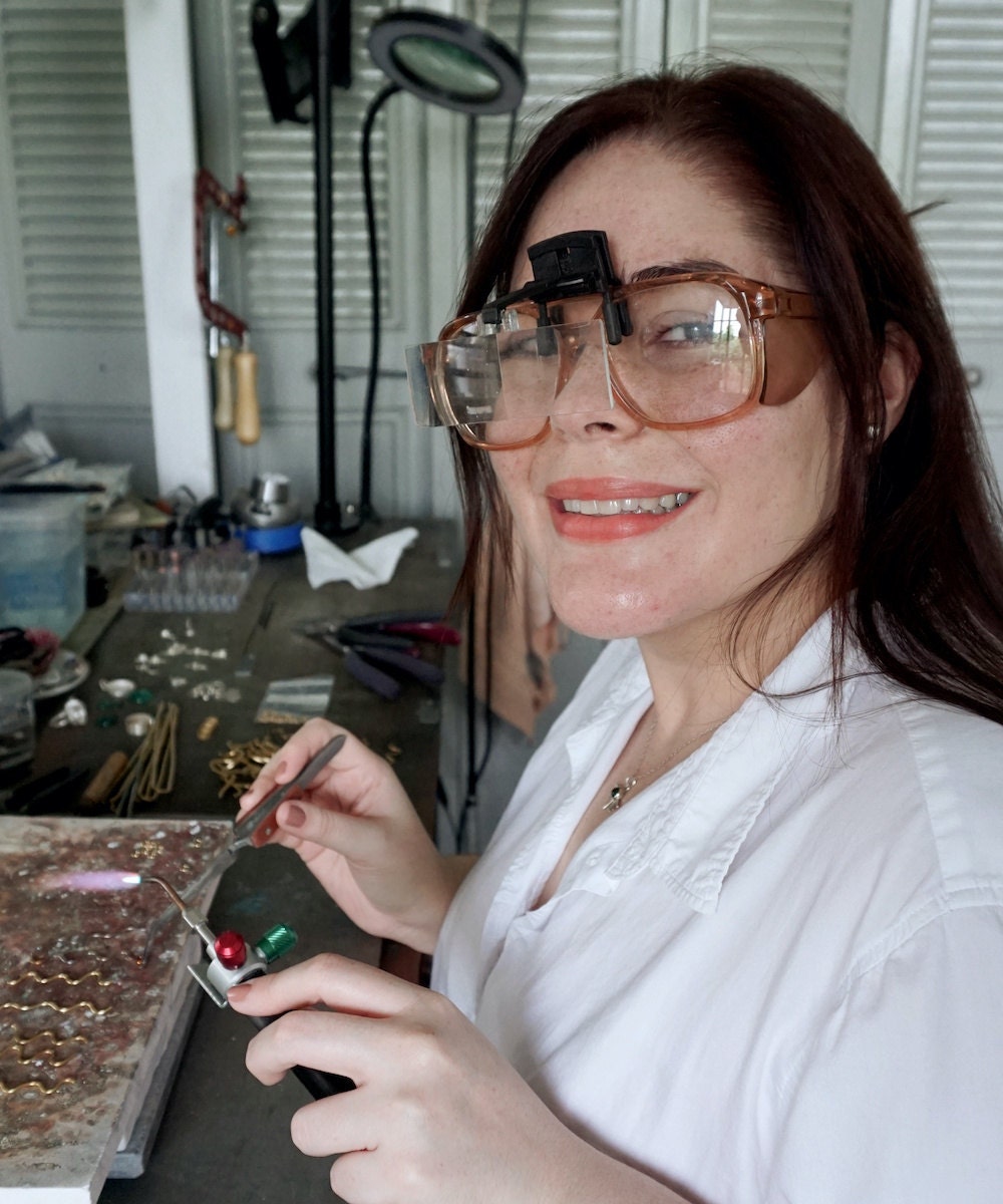 Aleishla smiling and holding a blowtorch in her studio.