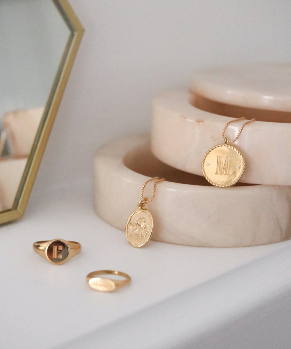 Assorted engraved, personalized gold signet rings and necklace pendants from EVREN, displayed in a marble jewelry box.