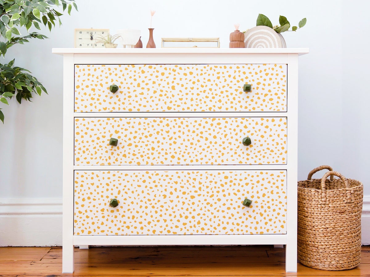 A dresser decorated with peel-and-stick yellow speckled wall paper.