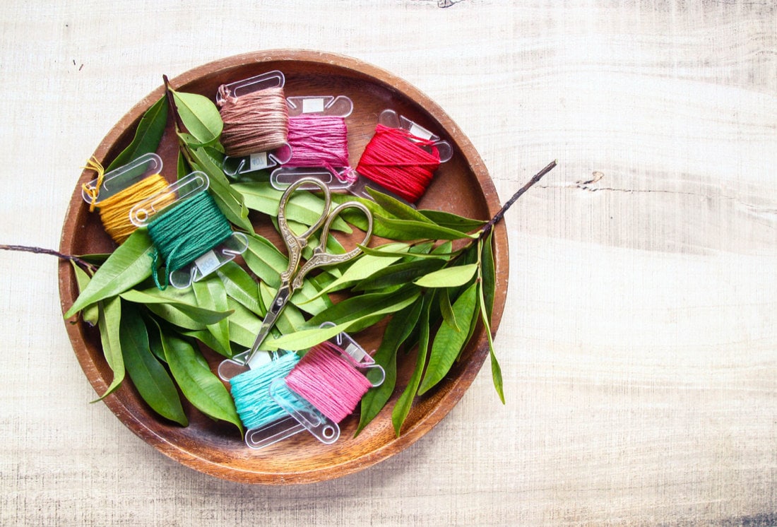 A wooden bowl full of colorful embroidery floss and a pair of embroidery scissors