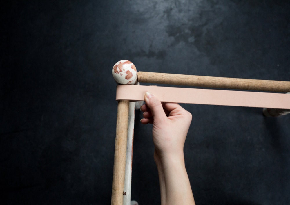 Looping one end of a leather strap around the stool's frame with 1 inch of overlap