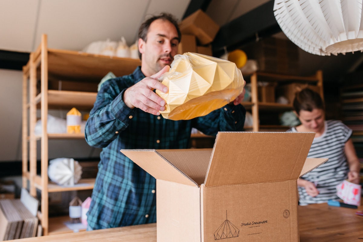 Kenneth places a finished yellow lampshade into a cardboard box for shipping