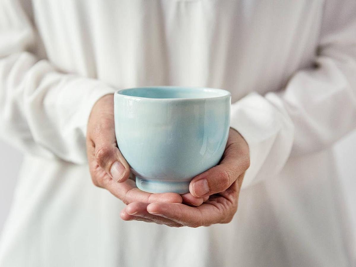 Closeup of a woman holding a blue teacup from Odaka in the palms of her hands.