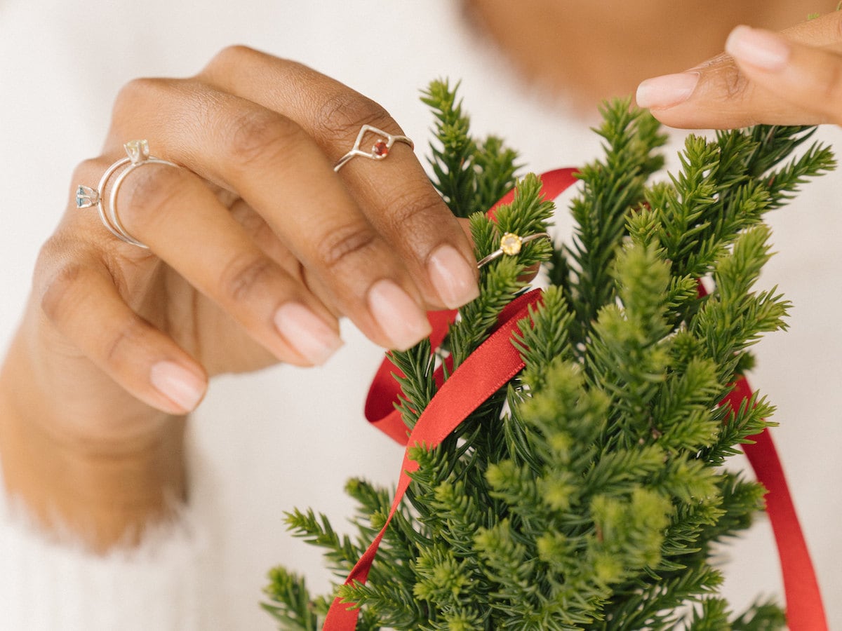 A woman wearing gemstone rings from Anne Swain Jewelry decorates an evergreen with red ribbon.