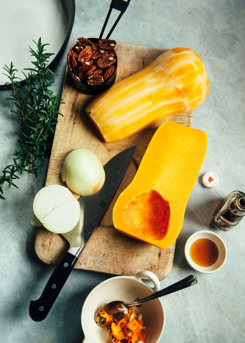 Halved butternut squash and onion laid on a cutting board, ready for slicing