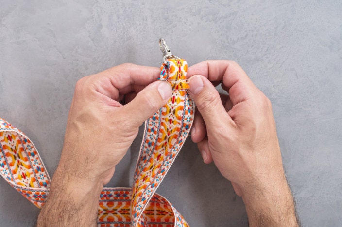 The short end of the trim that's through the swivel clasp is folded over and basted onto the backside of the strap near the edge